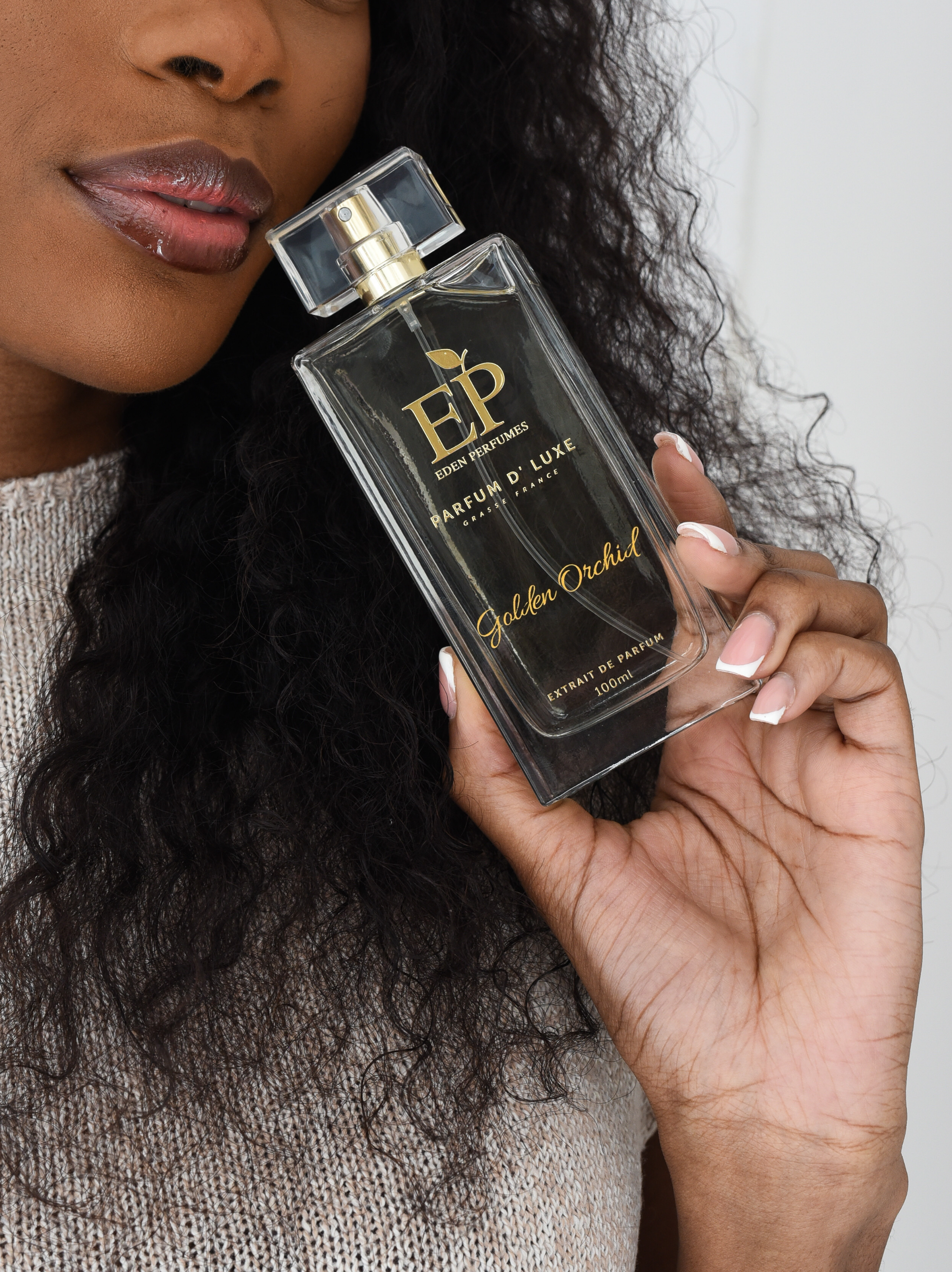 Woman holding an Eden Perfume bottle labeled 'Golden Orchid' with a clear cap.
